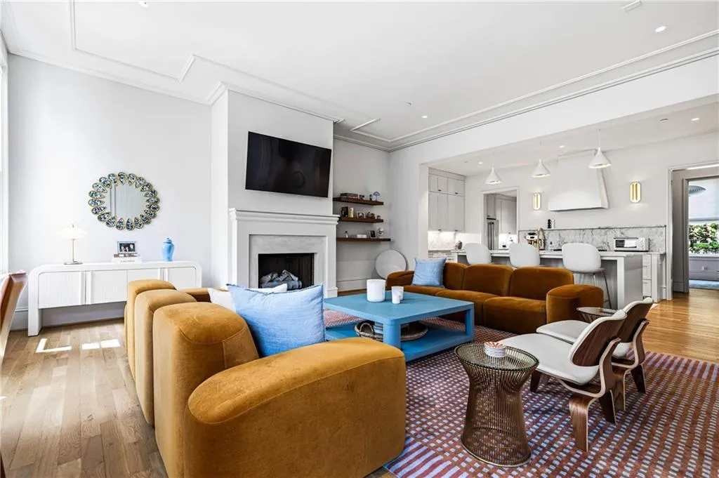 Open-concept living area featuring wood-finish flooring, a white mantel fireplace, extensive crown molding, a built-in kitchen island with seating, and integrated kitchen cabinetry