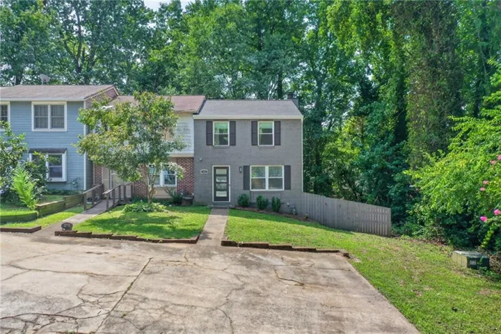 Grey brick exterior with black shutters, mature landscaping, and a fenced perimeter