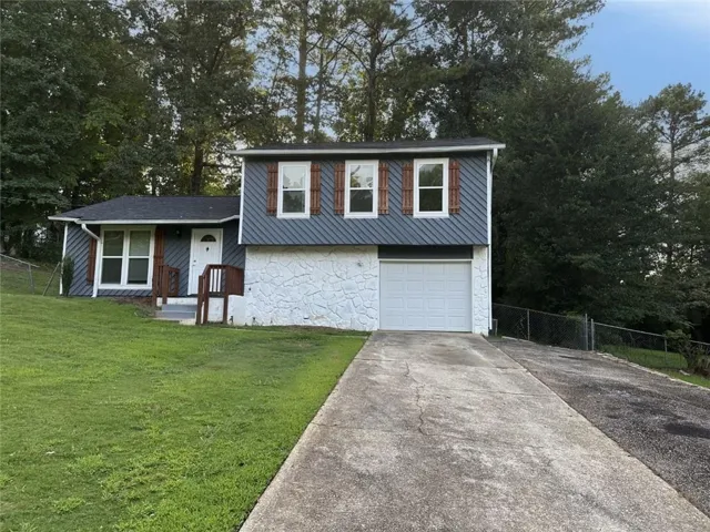 Split-level exterior featuring white painted stone, gray siding, and a white garage door