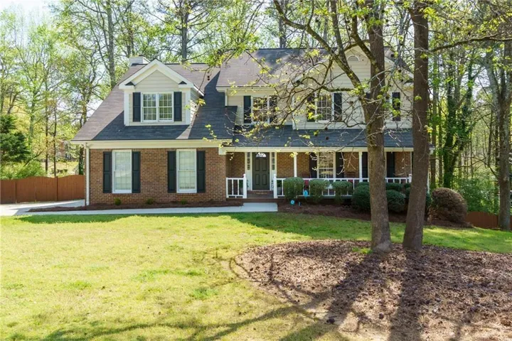 View of front of home with a porch, brick siding, a chimney, and roof with shingles