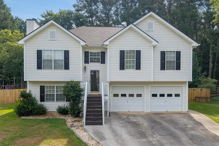 White vinyl siding exterior with black window shutters, a prominent front entry staircase, and a two-car garage
