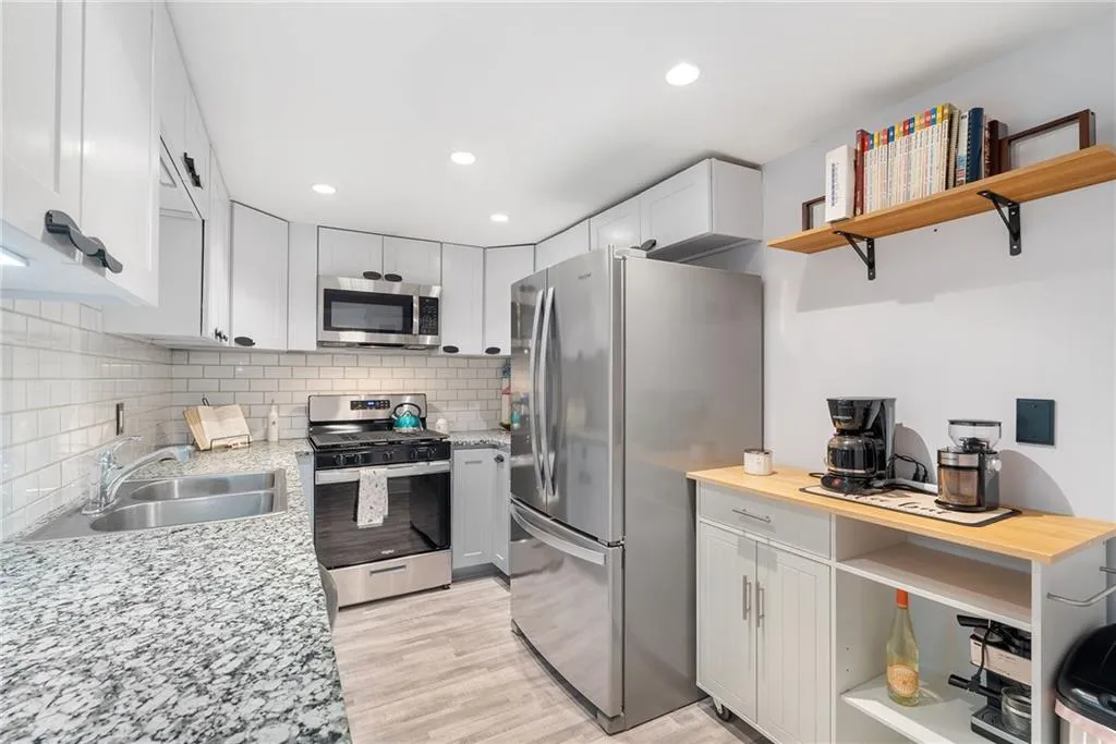 Kitchen featuring sink, appliances with stainless steel finishes, white cabinets, light stone countertops, and backsplash