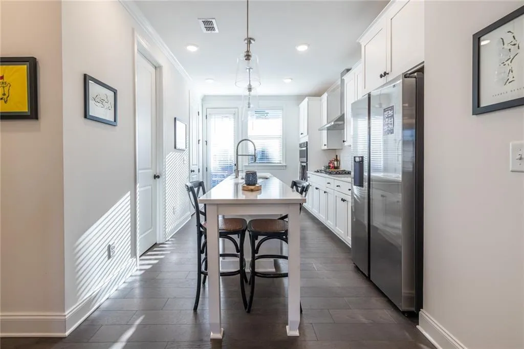 Kitchen with stainless steel appliances, white cabinetry, a breakfast bar, a kitchen island with sink, and hanging light fixtures