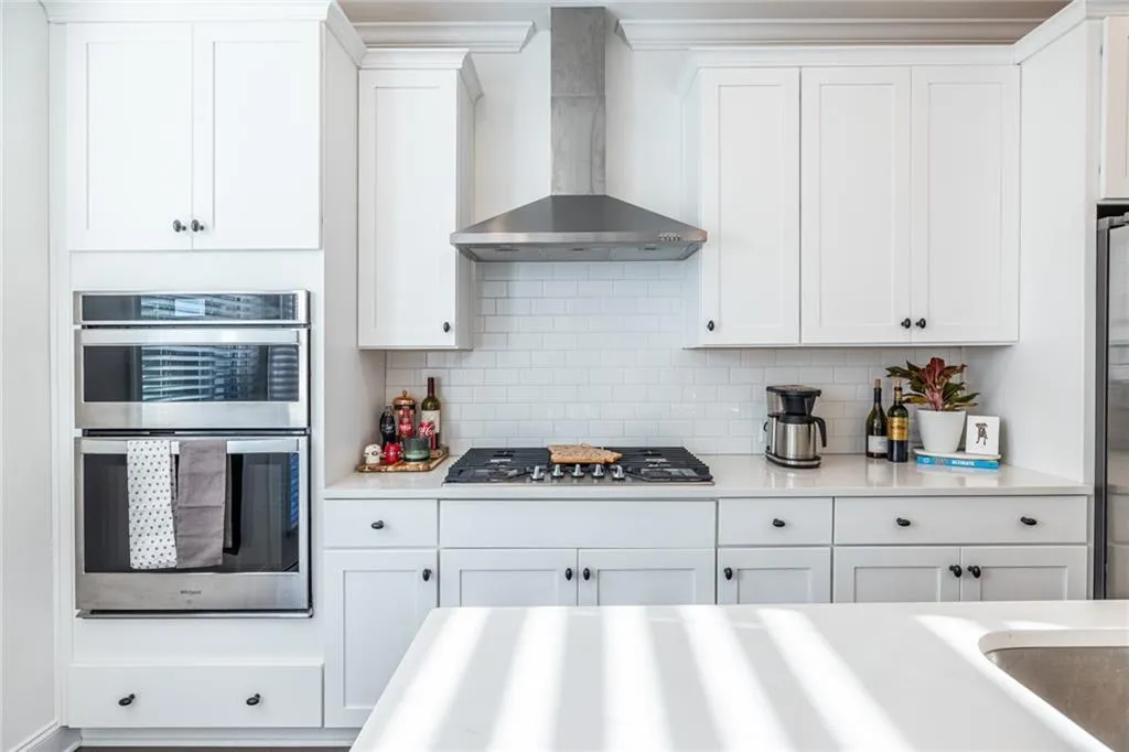 Kitchen with wall chimney range hood, appliances with stainless steel finishes, white cabinets, and tasteful backsplash