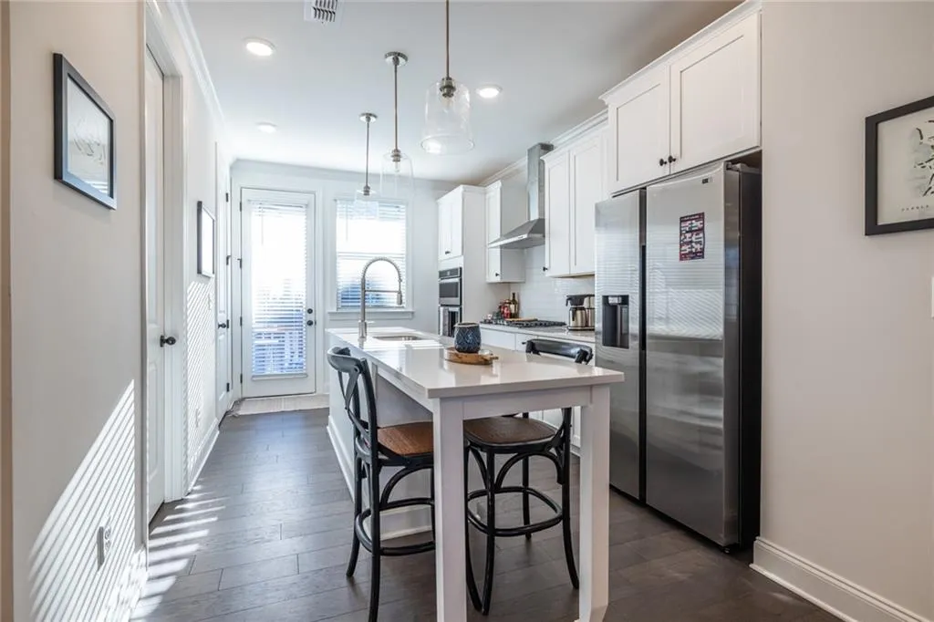 Kitchen with stainless steel appliances, wall chimney range hood, an island with sink, white cabinetry, and light countertops