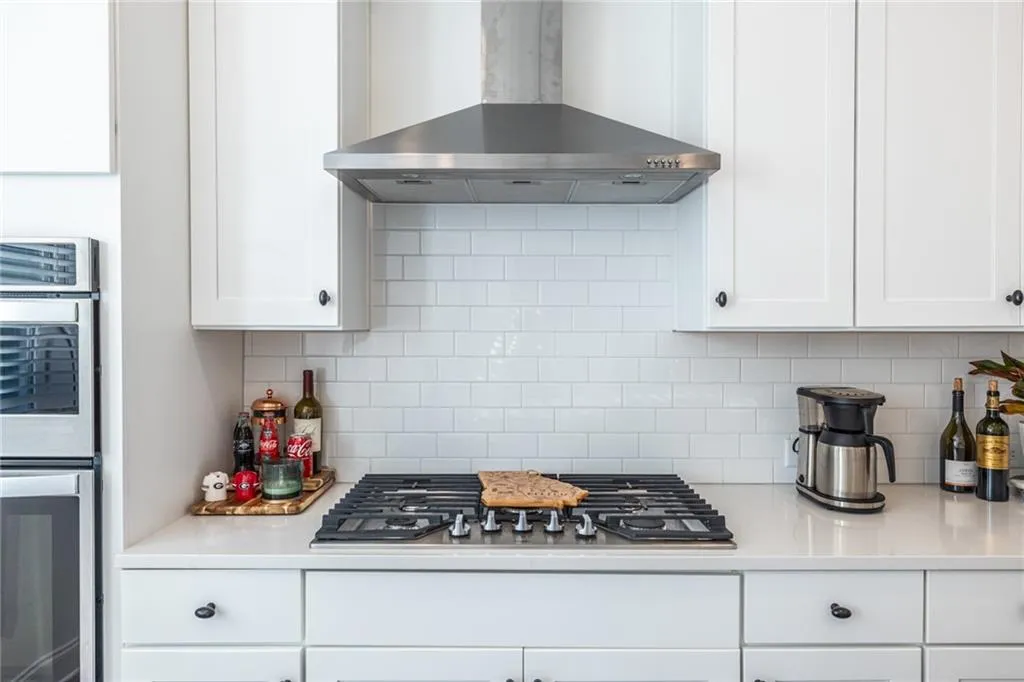 Kitchen with wall chimney range hood, stainless steel appliances, light countertops, and white cabinets