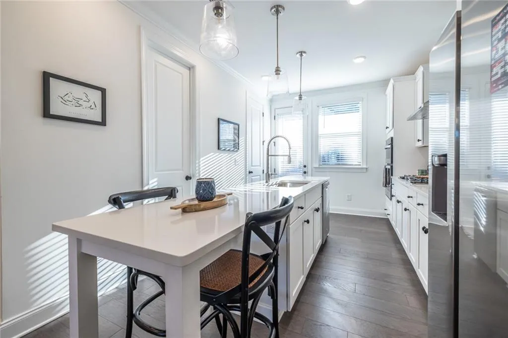 Kitchen featuring white cabinetry, light countertops, crown molding, pendant lighting, and a center island with sink
