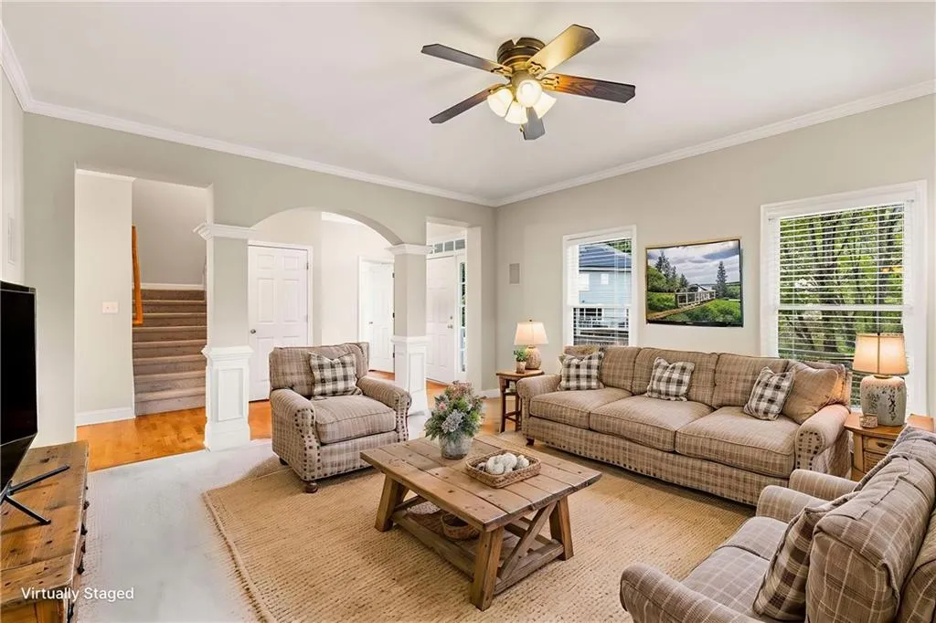 Living area featuring crown molding, decorative columns, wood finished floors, arched walkways, and stairway