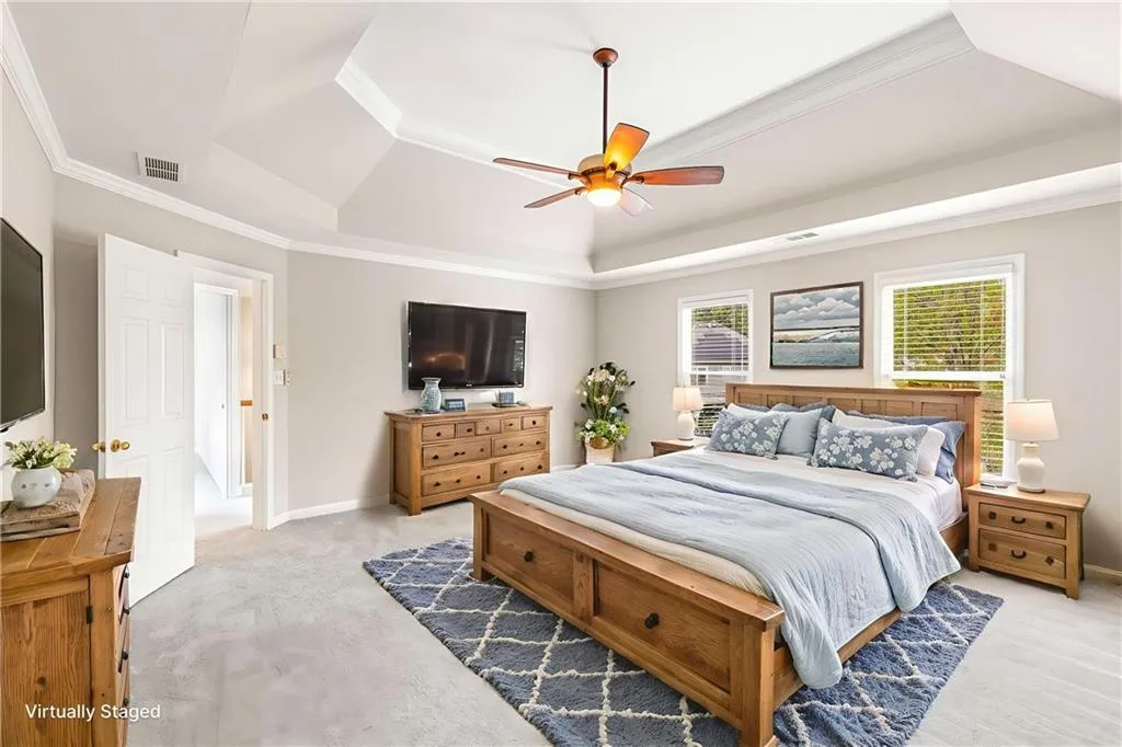 Bedroom with a tray ceiling, ornamental molding, light carpet, and ceiling fan