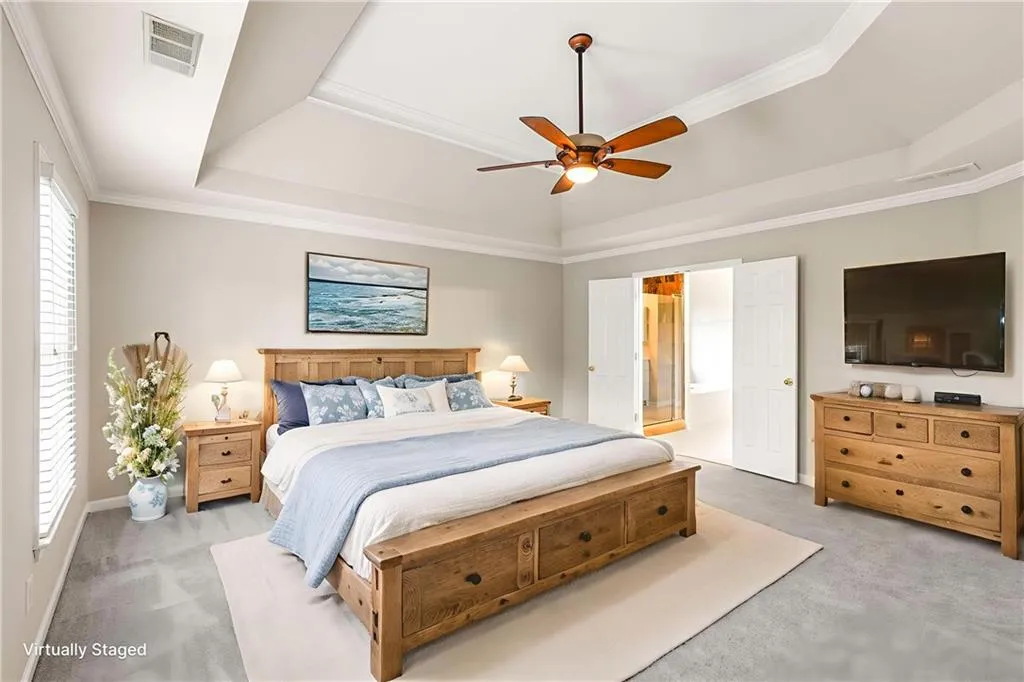 Carpeted bedroom with a raised ceiling, crown molding, ceiling fan, and connected bathroom