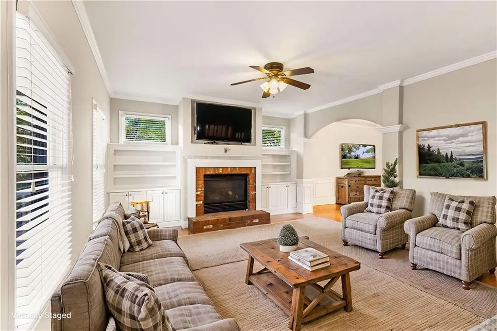 Living room featuring ornamental molding, a brick fireplace, arched walkways, built in features, and wood finished floors
