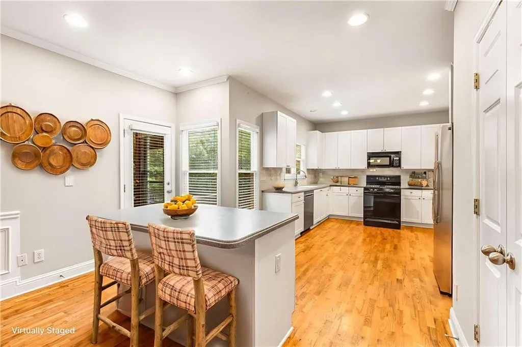 Kitchen with a kitchen bar, black appliances, backsplash, light wood-style floors, and white cabinets