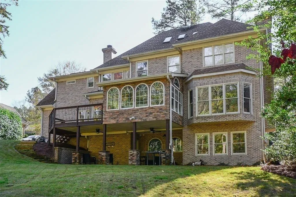Rear view of property with a chimney, a yard, a wooden deck, ceiling fan, and brick siding