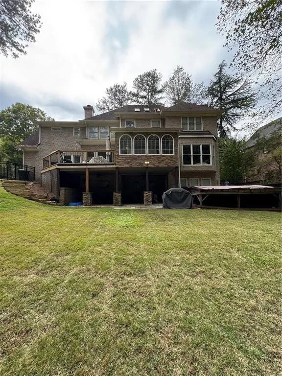 Back of house featuring a yard, a chimney, a wooden deck, and a balcony