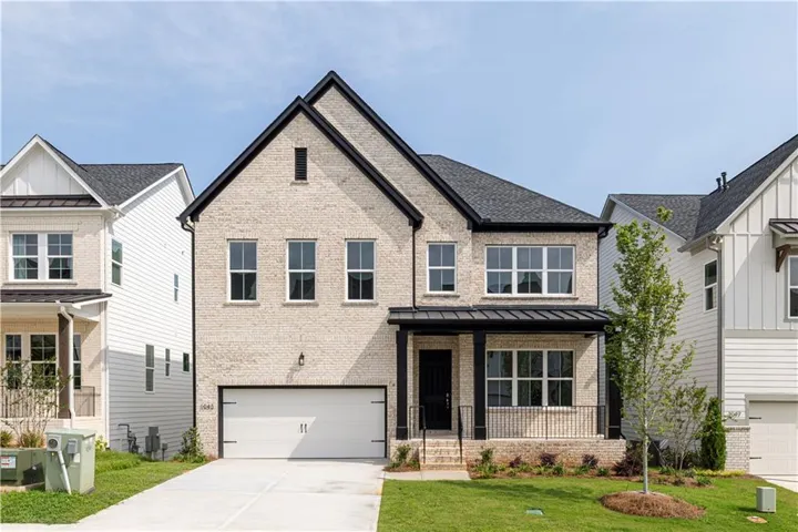 Striking brick Toll Brothers Sweetwater plan featuring a symmetrical gabled facade with multi-pane  windows, black metal roof accents, and a welcoming brick entry and covered porch
