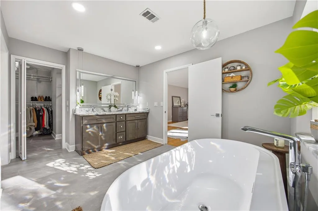 Spa-like primary bath featuring a freestanding soaking tub, double vanity with LED backlit mirror, and large walk-in closet