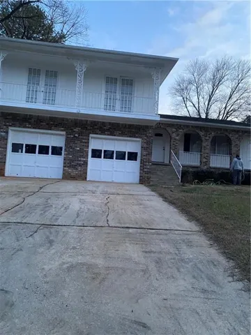 View of front facade featuring an attached garage, a balcony, concrete driveway, and brick siding