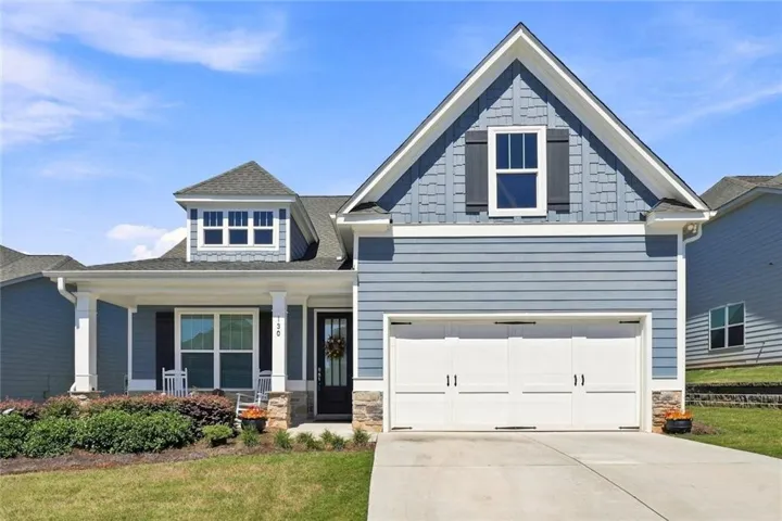 Expansive front facade featuring blue horizontal siding, stone accents, a covered porch with white columns, a two-car garage, and a dormer with shake siding