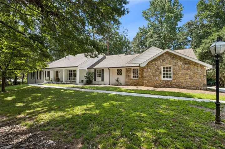Single-story residence featuring a stone and white brick exterior, covered front porch with columns, and a paved walkway