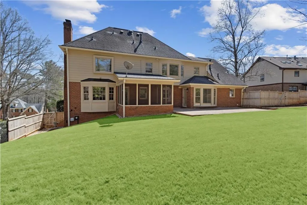 Rear view of house with brick siding, a fenced backyard, a chimney, and a lawn