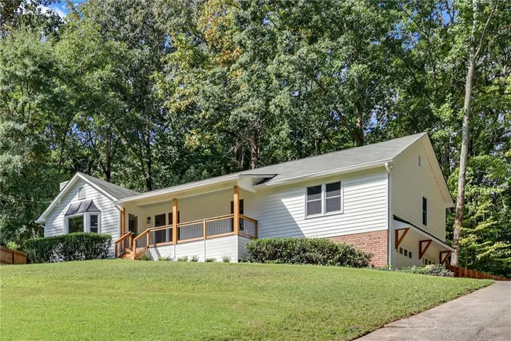 White siding exterior with brick accents, covered porch with wood railing, bay window, and gabled rooflines
