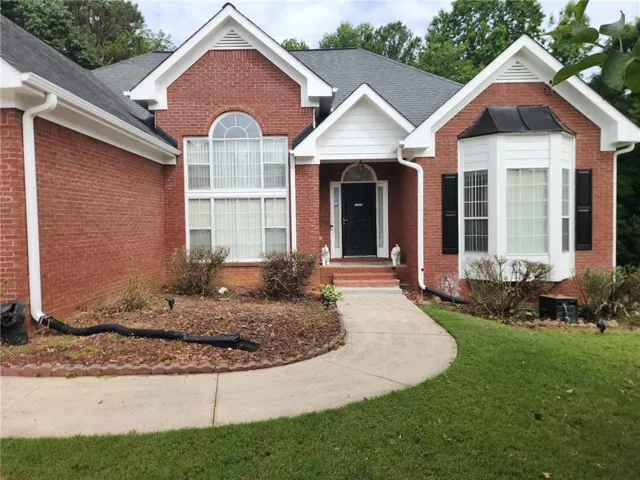 Brick exterior featuring a curved concrete walkway, gabled rooflines, an arched transom window, and a bay window with dark shutters