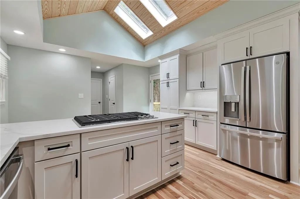 Kitchen with lofted ceiling with skylight, white cabinetry, light hardwood / wood-style flooring, light stone counters, and appliances with stainless steel finishes