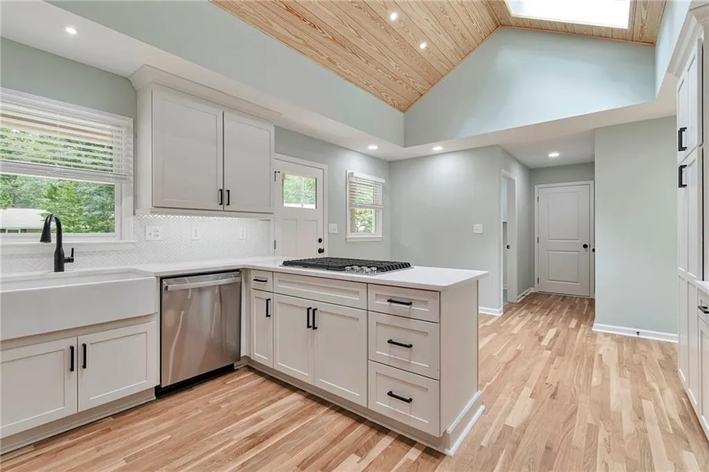 Kitchen featuring backsplash, light hardwood / wood-style floors, stainless steel appliances, kitchen peninsula, and white cabinetry