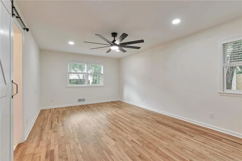 Unfurnished room with a barn door, ceiling fan, and light hardwood / wood-style floors