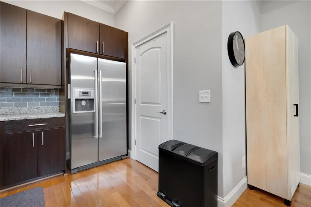 Kitchen with stainless steel refrigerator with ice dispenser, dark brown cabinetry, light wood finished floors, backsplash, and ornamental molding