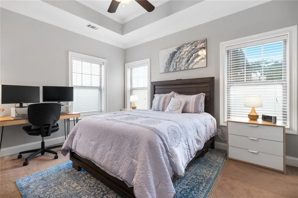 Bedroom featuring light carpet, an office area, multiple windows, and ornamental molding