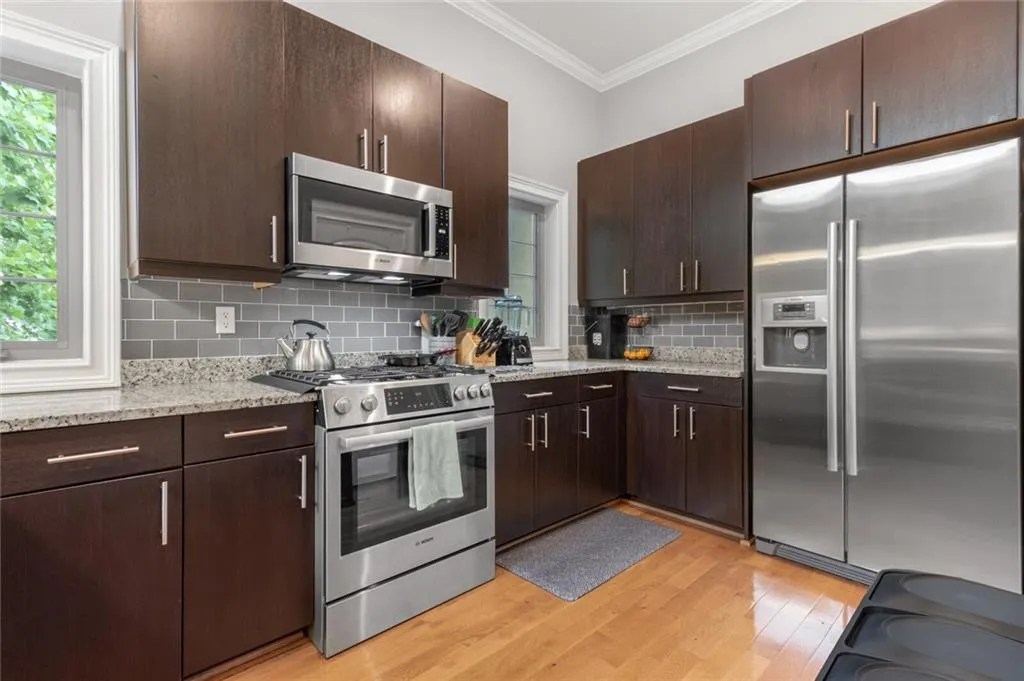 Kitchen with appliances with stainless steel finishes, dark brown cabinetry, ornamental molding, light wood-style flooring, and light stone counters