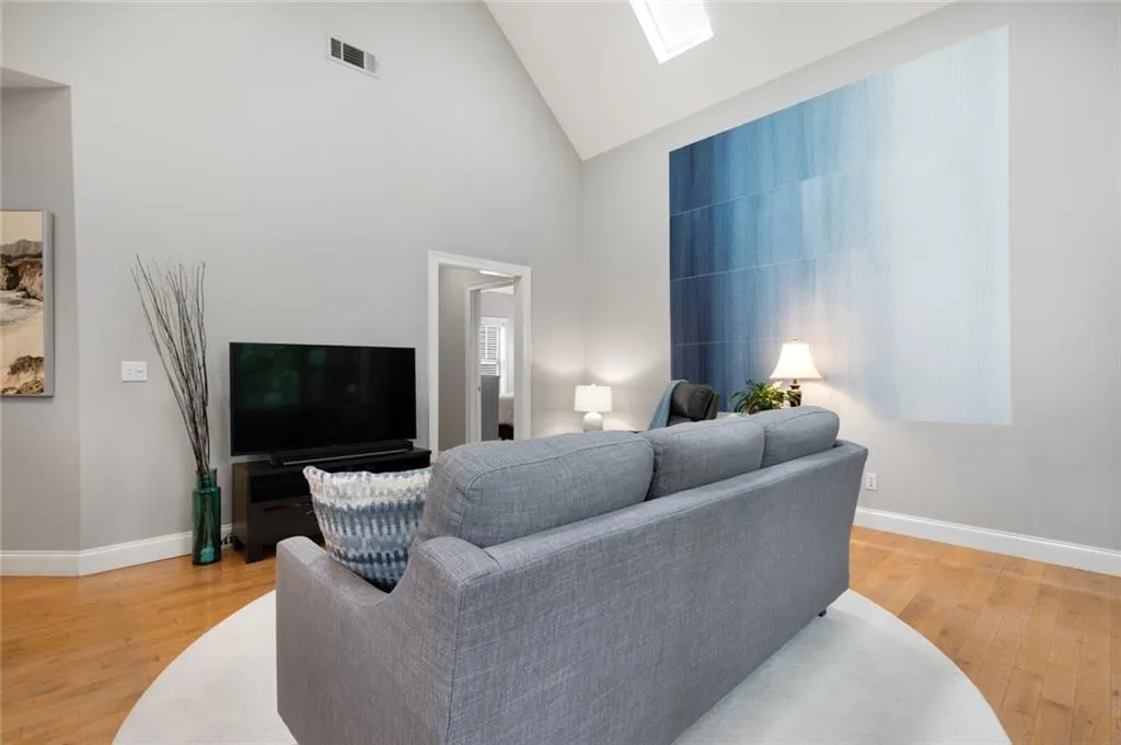 Living room with high vaulted ceiling, light wood-style flooring, and a skylight
