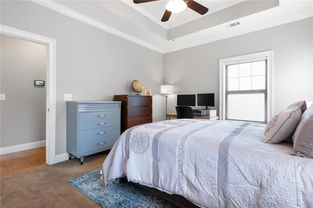 Carpeted bedroom featuring a tray ceiling, ornamental molding, and ceiling fan