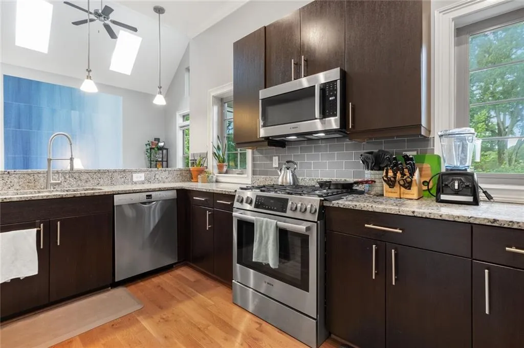 Kitchen with dark brown cabinets, vaulted ceiling, appliances with stainless steel finishes, light wood-style floors, and hanging light fixtures