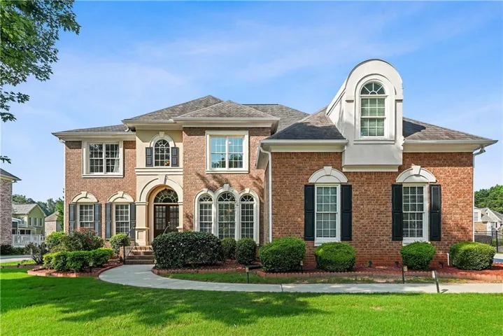 Brick exterior residence featuring an arched portico, multiple gabled rooflines, and a prominent dormer window