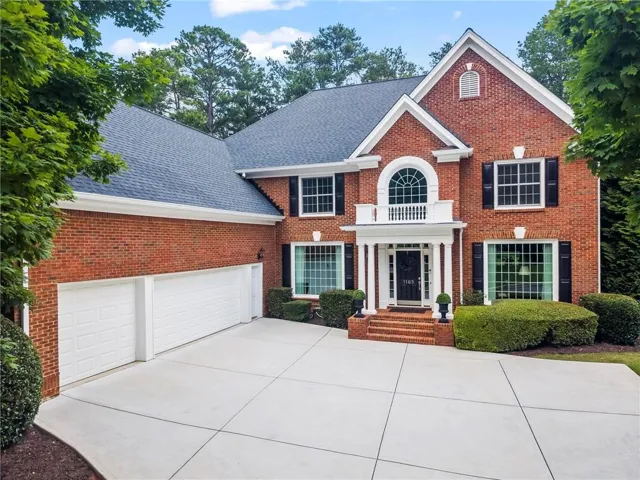 Traditional brick residence featuring a prominent portico entrance with white columns and a second-story arched window with a balcony