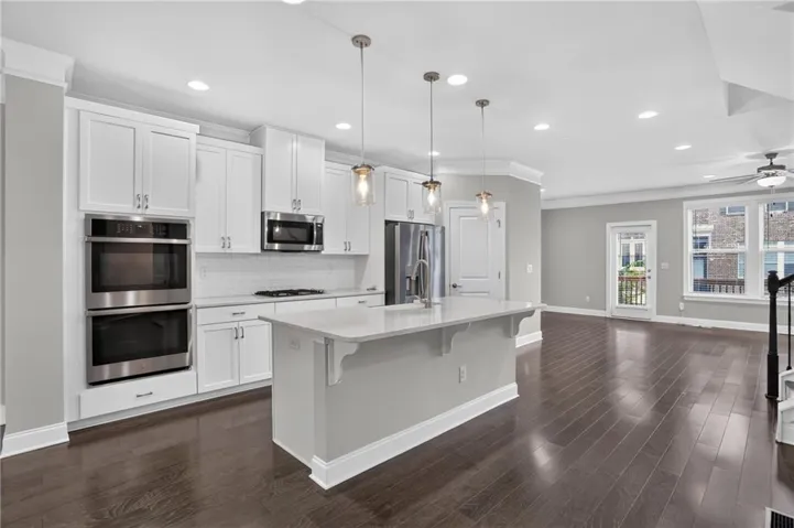 Kitchen with white shaker cabinetry, stainless steel double ovens, a central island with countertop seating, wood-finish flooring, and recessed lighting
