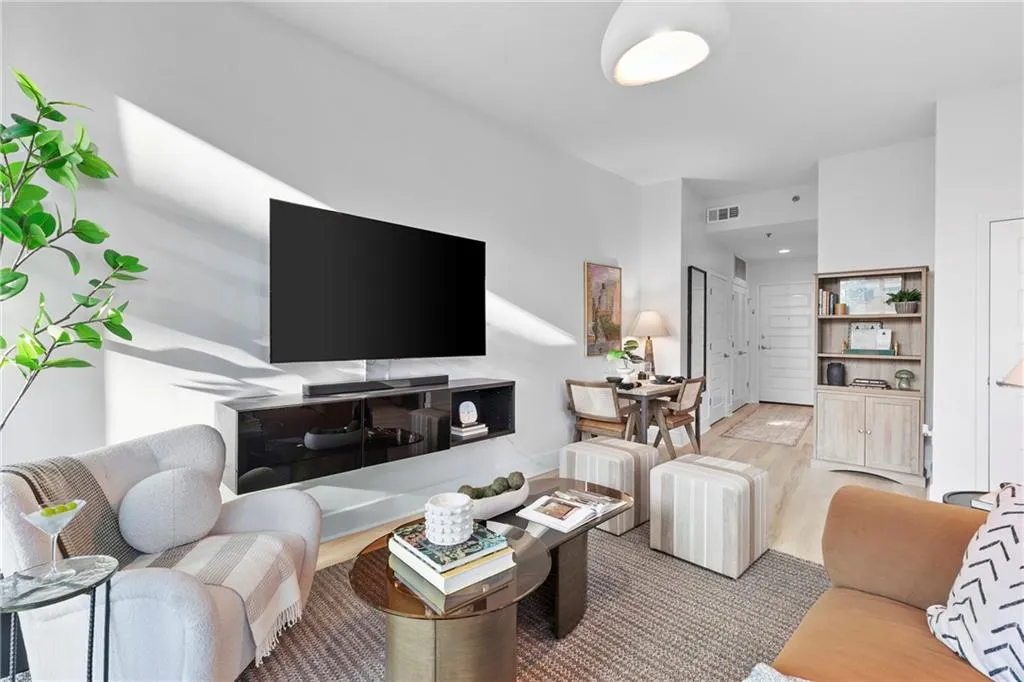 Living space featuring a wall-mounted media console, light-toned wood-finish flooring, and a built-in shelving unit with lower cabinetry