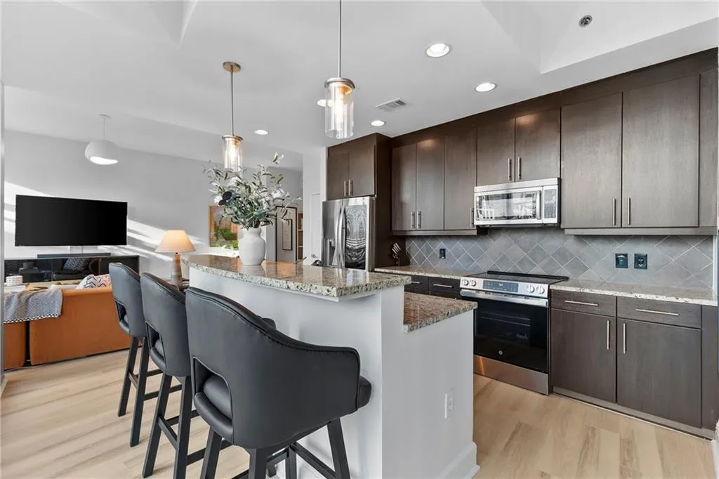 Contemporary kitchen featuring dark wood-finish cabinetry, stainless steel appliances, a diamond-patterned tile backsplash, a granite-finish island, and wood-finish flooring