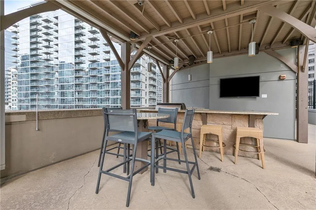 Covered outdoor area featuring a built-in stone-finish bar with a light-toned countertop, integrated outdoor television, and exposed beam ceiling structure