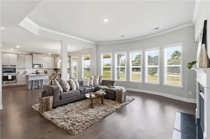 Open concept living space featuring wood-finish flooring, a white mantel, and extensive crown molding