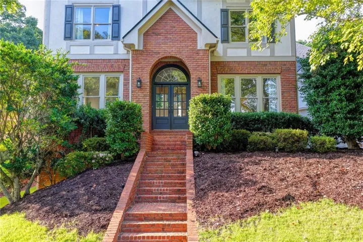 Brick exterior featuring an arched entryway with double doors, symmetrical windows, and a gabled roofline