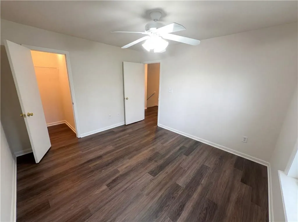Unfurnished bedroom featuring dark wood-type flooring, a ceiling fan, and a walk in closet