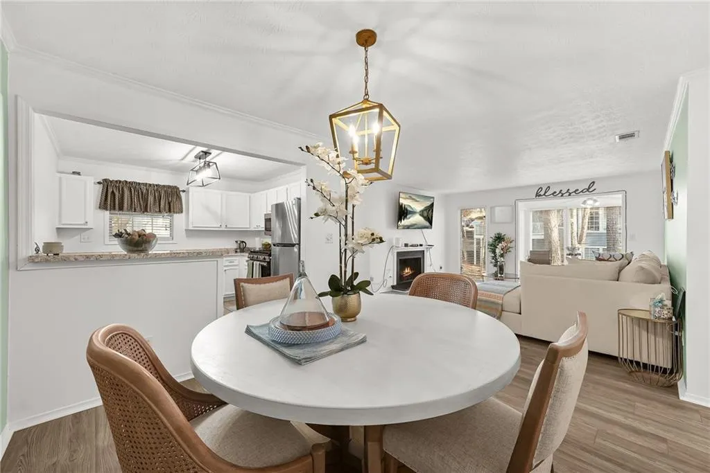 Dining space with a lit fireplace, light wood-style flooring, crown molding, and a chandelier