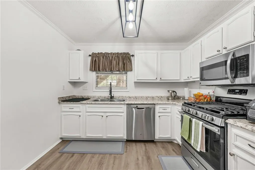 Kitchen with stainless steel appliances, white cabinetry, light wood-style floors, ornamental molding, and light stone countertops