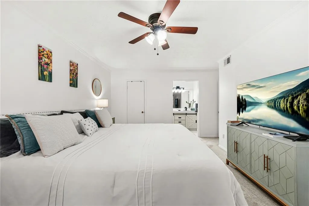 Bedroom featuring ornamental molding, light colored carpet, ceiling fan, ensuite bath, and a closet