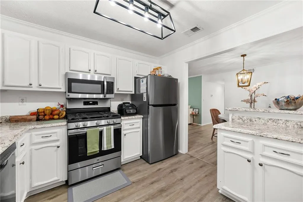 Kitchen with stainless steel appliances, light stone countertops, white cabinetry, and ornamental molding