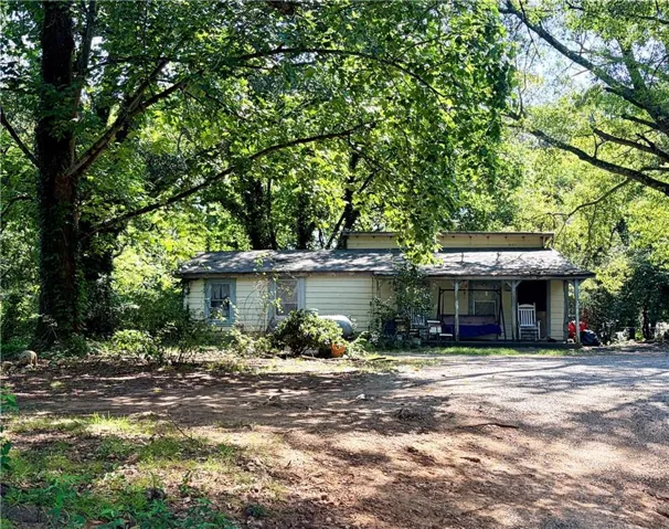 Single-story residence featuring light-colored siding, a covered front porch, and multiple mature trees providing natural shading