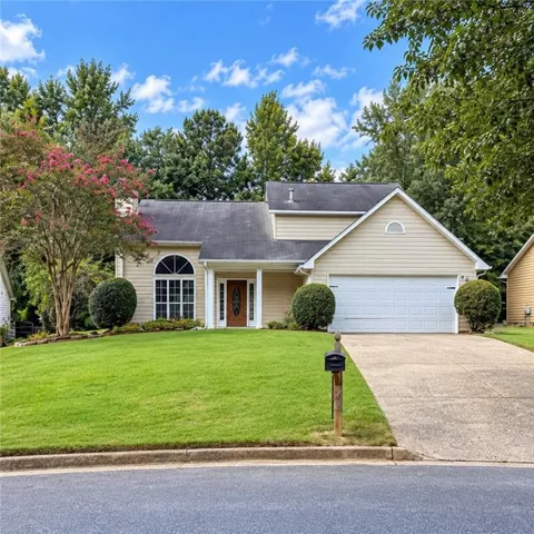 Traditional architecture with tan siding, a two-car garage, a covered entry, an arched window